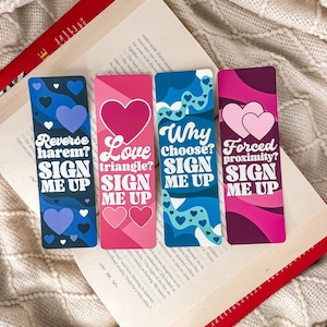 May include: Four colourful bookmarks with text and heart designs. The bookmarks feature phrases such as "Reverse harem?", "Love triangle?", "Why choose?" and "Forced proximity?" with "Sign me up" below.
