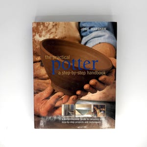 May include: A book titled The Practical Potter: A Step-by-Step Handbook by Josie Warshaw. The cover features a brown ceramic bowl being held, with smaller inset images of pottery projects and the subtitle A Comprehensive Guide to Ceramics.