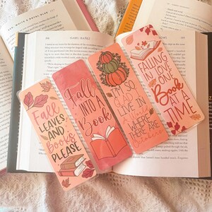 Könnte beinhalten: Vier rosa und orangefarbene Lesezeichen mit Herbstmotiven. Die Lesezeichen zeigen Illustrationen von Kürbissen, Blättern und Büchern. Der Text auf den Lesezeichen lautet: "Fall Leaves and Books Please", "Fall into a Book", "I'm so glad I live in a world where there are Octobers", und "Falling in love one book at a time".