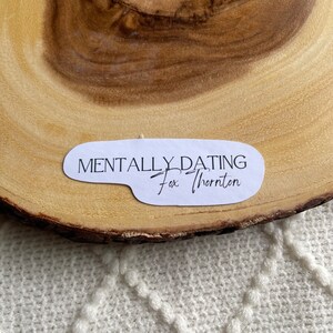 Puede incluir: Pegatina blanca con texto negro que dice "Mentally Dating Fox Thornton" sobre una superficie de madera.