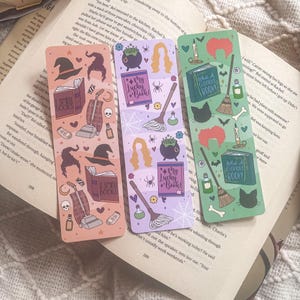 May include: Three colorful bookmarks with a Halloween theme. The bookmarks feature illustrations of witches, cats, brooms, cauldrons, and books. The text on the bookmarks reads "My Lucky Book!" and "What a Glorious Book!"