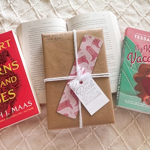 May include: A brown paper-wrapped book with a pink and white bookmark and a white gift tag that says "This Book Belongs To".