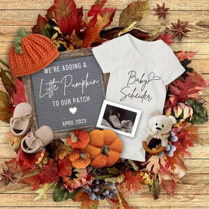 Pode incluir: Um anúncio de nascimento com tema de outono com um quadro de letras que diz "We're adding a little pumpkin to our patch April 2023". Há um chapéu de abóbora de crochê, botinhas e um enfeite de abóbora. Também está incluído um macacão branco com o texto "Baby Schneider" e uma imagem de ultrassom.