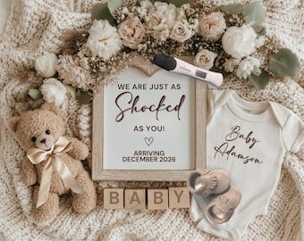 May include: A pregnancy announcement featuring a framed sign with the text "We are just as shocked as you!" and "Arriving December 2026." The scene includes a teddy bear, baby shoes, a onesie, and wooden blocks spelling "BABY."