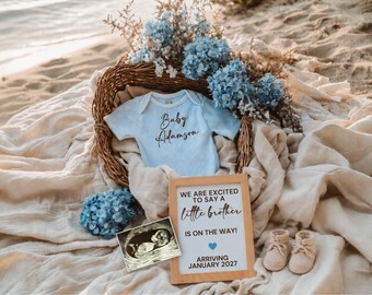 May include: A baby announcement scene with a light blue onesie that says "Baby Adamson" in script. A sign reads "We are excited to say a little brother is on the way! Arriving January 2027." The scene includes baby booties, an ultrasound image, and blue flowers.