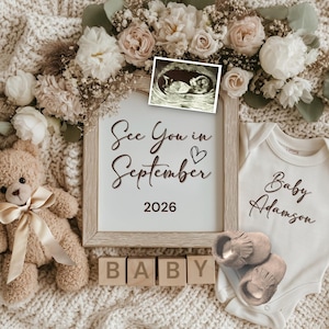 Puede incluir: Anuncio de bebé con un oso de peluche, una imagen de ultrasonido y un letrero que dice "See You in September 2026". Un body blanco con "Baby Adamson" y zapatos de bebé también están presentes. La escena está decorada con flores.