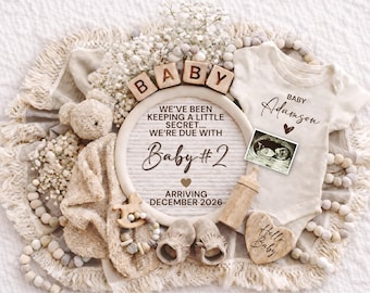 May include: A neutral-toned baby announcement with a teddy bear, baby clothes, and ultrasound image. The announcement includes the text "Baby #2" and "Arriving December 2026". A heart-shaped wooden sign says "Hello Baby".
