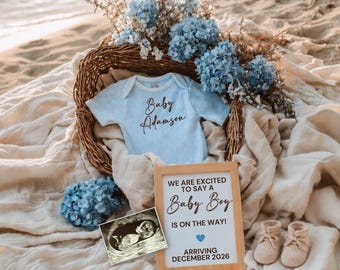 May include: A baby announcement scene with a light blue onesie that says "Baby Adamson" in script. A sign reads "We are excited to say a Baby Boy is on the way! Arriving December 2026." The scene includes baby booties, an ultrasound image, and blue flowers.