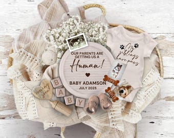 May include: A baby announcement gift basket with a wooden sign that reads "Our parents are getting us a human! Baby Adamson July 2025". The basket also includes a baby onesie that says "My siblings have paws" with a picture of a dog, a wooden heart that says "coming soon", and a baby bottle.