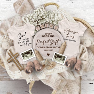 May include: A baby shower gift basket with two pink baby onesies, one with the text "God knew our hearts needed you" and the other with the text "Adamson twins November 2024". The basket also includes a wooden sign with the text "Every good and perfect gift comes from above James 1:17", a wooden cross, two ultrasound pictures, and other baby items.