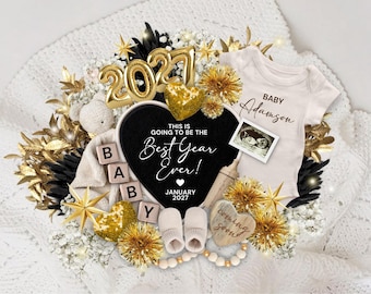 May include: A baby announcement set featuring a white onesie with 'Baby Adamson' text, a black heart sign reading 'This is going to be the best year ever! January 2027', gold '2027' balloons, baby booties, wooden letter blocks, and an ultrasound photo.