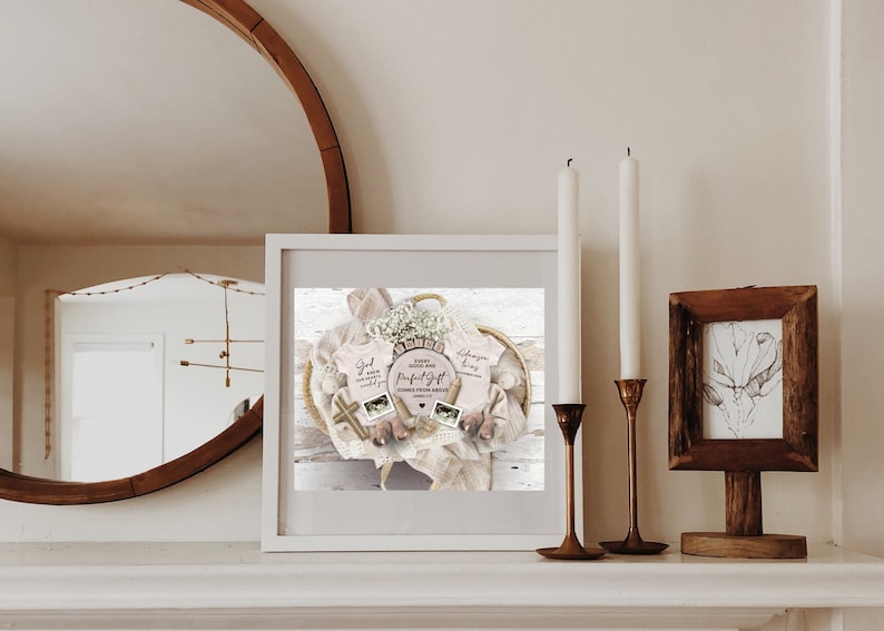 May include: A framed print of a baby shower gift basket with a white background. The basket contains two pink baby onesies, one with the text "God made you so wonderfully" and the other with the text "Ephesians 1:4", a small wooden cross, a white blanket, and a white flower arrangement. The text "Every good and perfect gift comes from above" is written on a wooden sign.