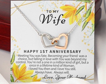May include: A silver necklace with two intertwined heart pendants, one silver and one rose gold. The necklace is displayed on a card with a floral design and the text "To My Wife Happy 1st Anniversary Meeting You was fate. Becoming your friend was a choice, but falling in love with You was beyond my control. You're not a one in a million kind of girl, but a once in a lifetime kind of Woman. I loved You then and I love You still. Always have. Always will. Love, Your Husband"