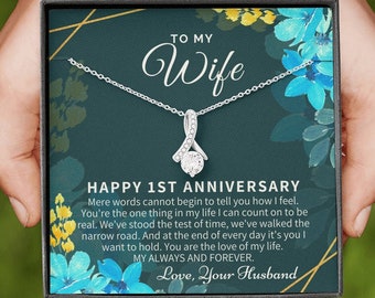 May include: A silver necklace with a sparkling stone pendant in a dark green box with a floral design. The box has the text "To My Wife" and "Happy 1st Anniversary" with a message about love and marriage.