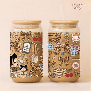 May include: Two glass tumblers with bamboo lids and straws, featuring a book-themed design. The tumblers have a light brown background with illustrations of books, bows, cherries, and the text "one more chapter" and "coffee & books".