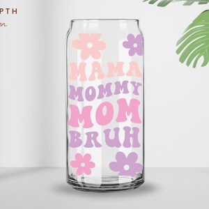 Puede incluir: Una lata de vidrio transparente con un dise&ntilde;o rosa y morado. La lata tiene las palabras "Mama", "Mommy", "Mom" y "Bruh" escritas en una fuente retro. Tambi&eacute;n hay flores rosas y moradas en la lata.