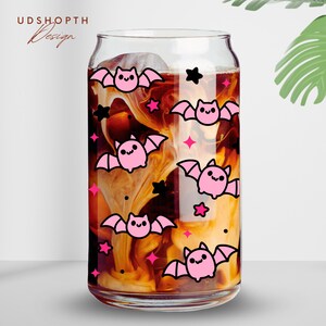 May include: A glass can with a pink and black bat pattern. The can is filled with a brown liquid and white swirls. The can has a clear glass lid.