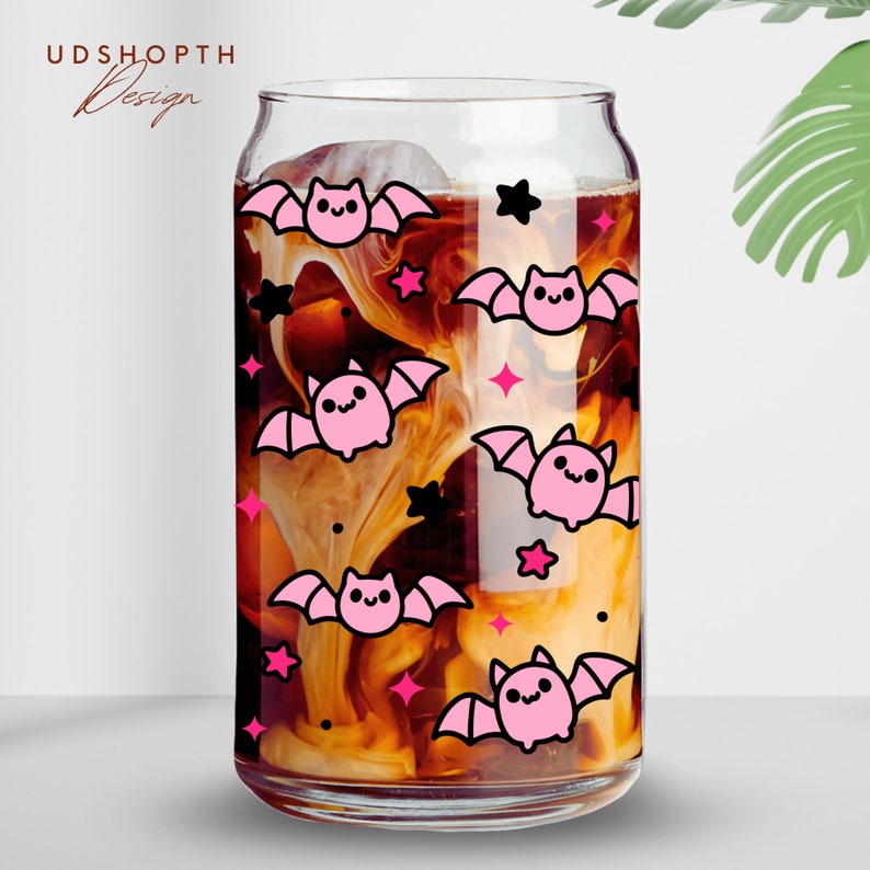 May include: A glass can with a pink and black bat pattern. The can is filled with a brown liquid and white swirls. The can has a clear glass lid.