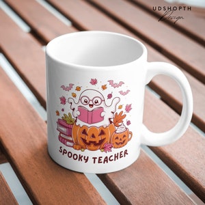Pu&ograve; includere: Tazza in ceramica bianca con un design di insegnante spettrale. Un fantasma con gli occhiali sta leggendo un libro mentre &egrave; seduto su una zucca. La tazza ha il testo "Spooky Teacher" stampato sul fondo.