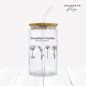 K&ouml;nnte beinhalten: Ein klares Glasgef&auml;&szlig; mit Bambusdeckel und Strohhalm. Das Gef&auml;&szlig; hat ein schwarzes Design mit der Aufschrift "Grandma's Garden where love grows" und zeigt vier stilisierte Blumen mit darauf geschriebenen Namen: "Blessing", "Linda", "Kamelia" und "Sophia".