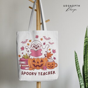 Pu&ograve; includere: Borsa tote in tela bianca con un design da insegnante spettrale. Un fantasma con gli occhiali sta leggendo un libro mentre &egrave; seduto in una zucca. Il fantasma &egrave; circondato da foglie autunnali, pipistrelli e una pila di libri. Il testo "Spooky Teacher" &egrave; stampato sotto l'immagine.