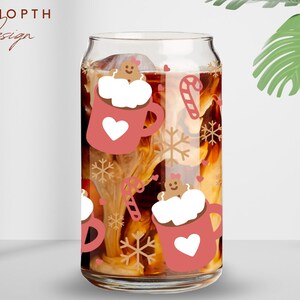 May include: A clear glass can-shaped cup filled with a beverage, featuring a festive design. The design includes pink mugs with white hearts, gingerbread men, snowflakes, and candy canes. The text "UDSHOPTH Design" is at the top left.