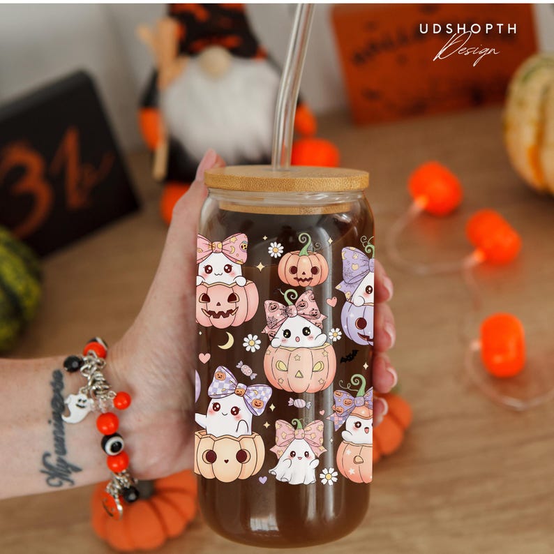 May include: A clear glass can-shaped tumbler with a bamboo lid and a glass straw. The tumbler is decorated with cute Halloween-themed illustrations of ghosts and pumpkins in pastel colors. The design includes the text "UDSHOPTH Design".