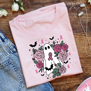 May include: Pink t-shirt with a white ghost wearing a pink ribbon surrounded by pink roses and bats. The text "UDSHOPTH Design" is in the top right corner of the image.