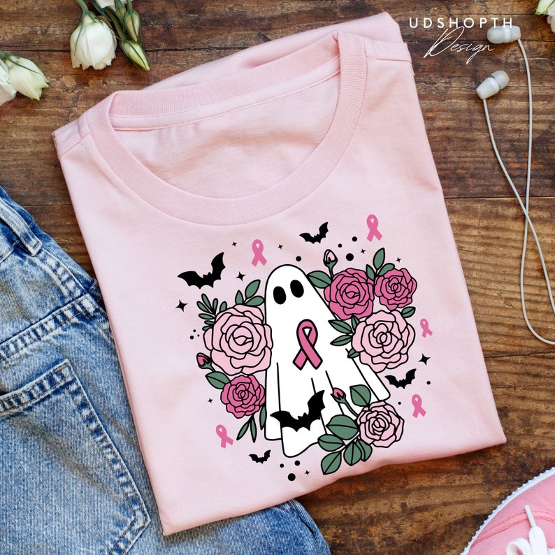 May include: Pink t-shirt with a white ghost wearing a pink ribbon surrounded by pink roses and bats. The text "UDSHOPTH Design" is in the top right corner of the image.
