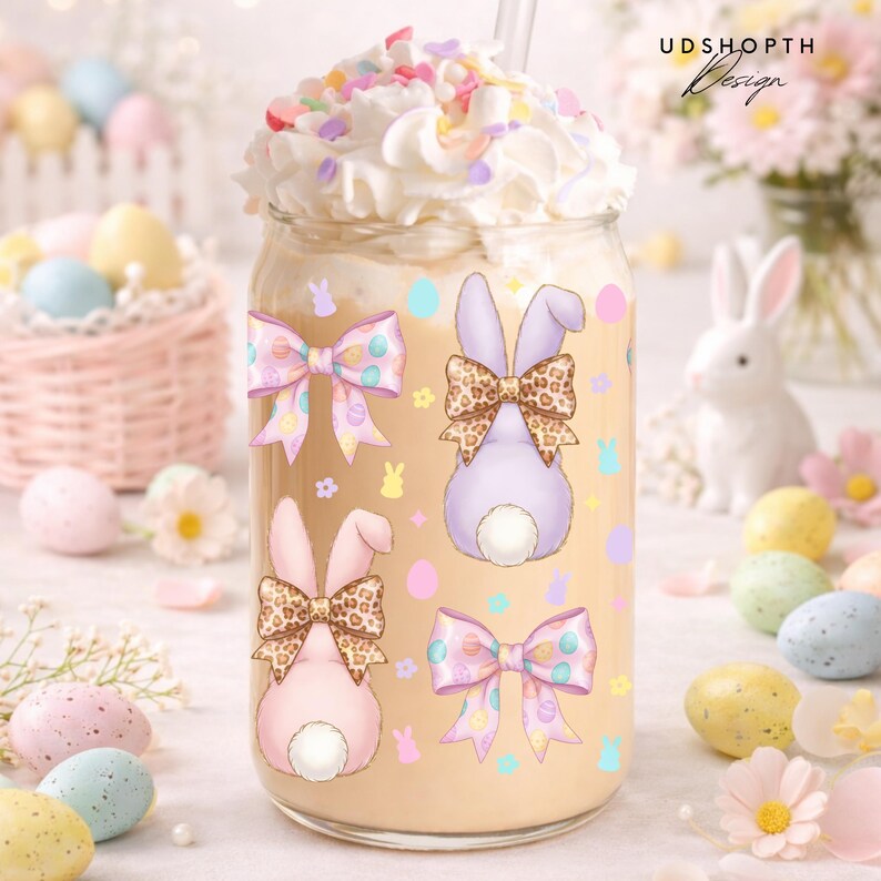 May include: A glass jar with a creamy beverage, topped with whipped cream and sprinkles. The jar is decorated with Easter bunny designs and bows. Pastel-colored Easter eggs and a basket are in the background. The text "UDSHOPTH Design" is visible.