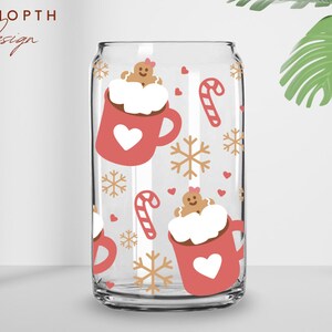 May include: Clear glass can-shaped cup with a festive holiday design. The cup features a repeating pattern of red mugs with white hearts, gingerbread men, candy canes, and snowflakes. The text "UDSHOPTH Design" is in the upper left corner.
