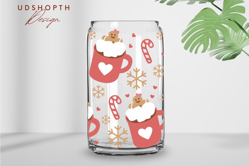 May include: Clear glass can-shaped cup with a festive holiday design. The cup features a repeating pattern of red mugs with white hearts, gingerbread men, candy canes, and snowflakes. The text "UDSHOPTH Design" is in the upper left corner.