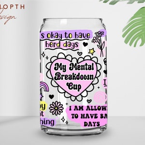 Peut inclure: Un verre transparent en forme de canette avec le texte "My Mental Breakdown Cup" dans un motif en forme de c&oelig;ur. La tasse est d&eacute;cor&eacute;e de divers gribouillis, notamment des fleurs, des &eacute;toiles et des arcs-en-ciel, et de phrases comme "It's okay to have herd days".