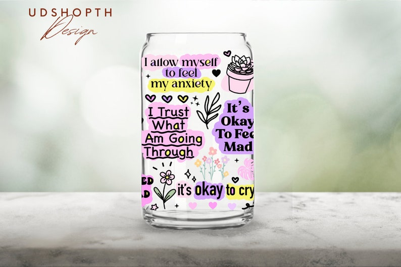 Peut inclure: Un verre transparent en forme de canette avec divers graphiques et textes color&eacute;s. Le texte comprend des phrases telles que "Je m'autorise &agrave; ressentir mon anxi&eacute;t&eacute;" et "C'est ok de pleurer". Le design pr&eacute;sente des c&oelig;urs, des fleurs et une plante succulente en pot.