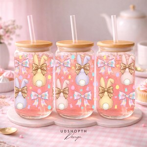 May include: Three glass tumblers with wooden lids and straws, filled with pink liquid. Each tumbler features a bunny design with a leopard print bow, surrounded by bows and Easter eggs. The text "UDSHOPTH Design" is at the bottom.