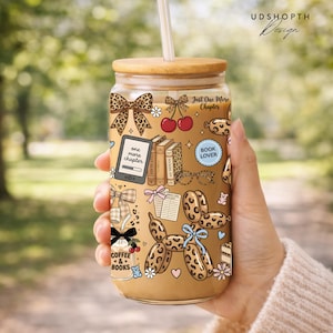 May include: A glass tumbler with a bamboo lid and straw, featuring a whimsical design with bows, books, cherries, and the text "Just One More Chapter." The tumbler has a leopard print pattern and the words "Coffee & Books."