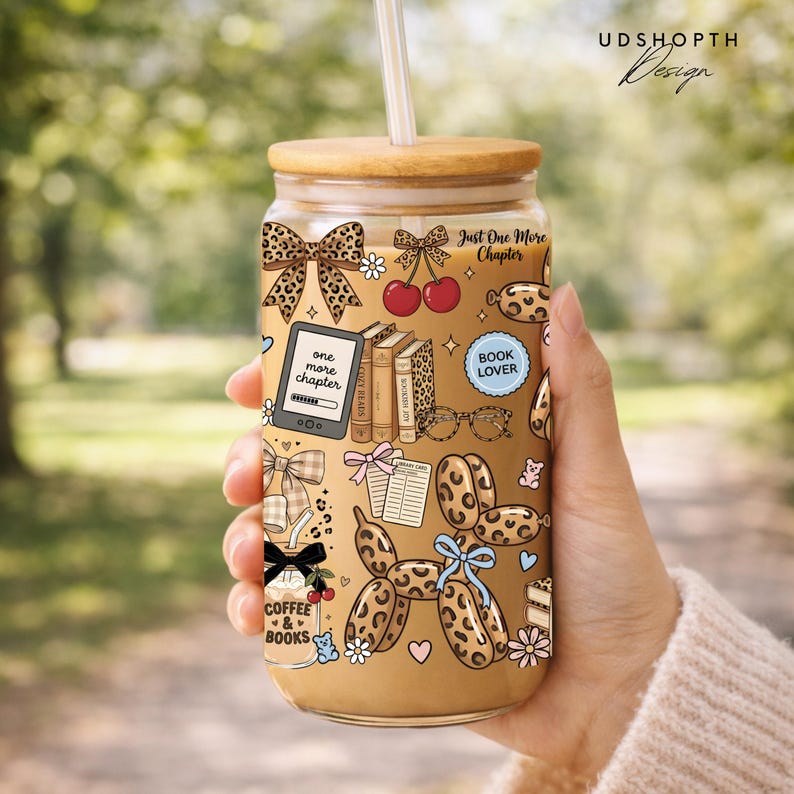 May include: A glass tumbler with a bamboo lid and straw, featuring a whimsical design with bows, books, cherries, and the text "Just One More Chapter." The tumbler has a leopard print pattern and the words "Coffee & Books."