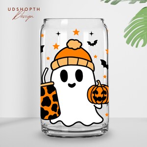 May include: A clear glass can with a white ghost wearing an orange and white hat holding a pumpkin and a black and white spotted beverage. The can has a black and white star pattern and bats.
