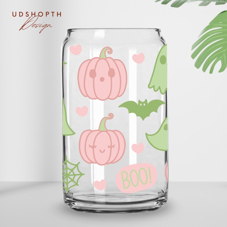 以下が含まれることがあります： ピンクとグリーンのハロウィーンデザインが施された透明なガラス製の缶。缶には、カボチャ、コウモリ、幽霊、ハート、クモの巣が描かれています。缶には「BOO！」の文字が印刷されています。