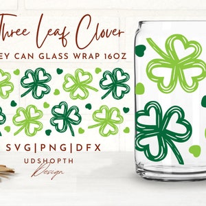 May include: A clear glass can with a green and white design of four-leaf clovers and hearts. The text "Three Leaf Clover" and "Libbey Can Glass Wrap 16oz" is printed on the image. The text "SVG|PNG|DFX" and "UDSHOPTH Design" is also printed on the image.