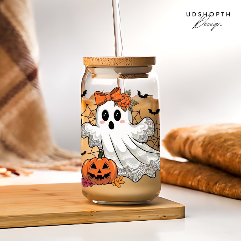 Pode incluir: Um frasco de vidro com tampa de madeira e um design tem&aacute;tico de Halloween. O design apresenta um fantasma branco com um la&ccedil;o, uma ab&oacute;bora e morcegos. O frasco est&aacute; cheio de um l&iacute;quido castanho.