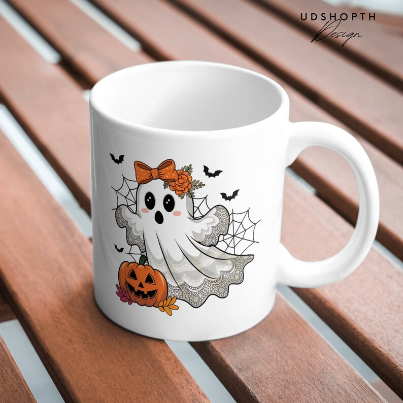 Pode incluir: Caneca de cer&acirc;mica branca com um fantasma de desenho animado fofo usando um la&ccedil;o e uma faixa de flores. O fantasma est&aacute; segurando uma ab&oacute;bora e h&aacute; morcegos e teias de aranha no fundo.
