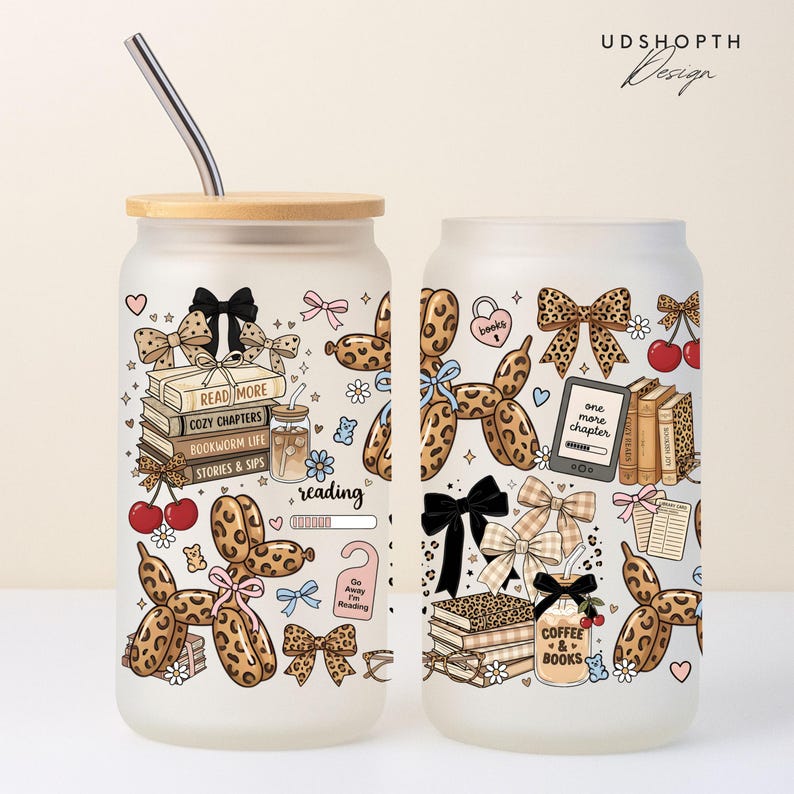May include: Frosted glass can-shaped tumbler with a bamboo lid and a stainless steel straw. The tumbler features a whimsical design with books, bows, cherries, and a balloon dog. The words "READ MORE", "COZY CHAPTERS", and "COFFEE & BOOKS" are visible.