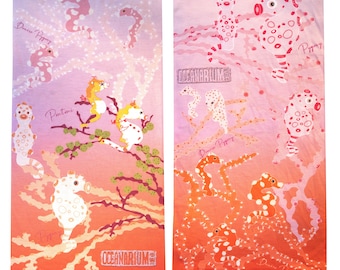 May include: Two beach towels with a seahorse design. The towels feature seahorses in various colors, including white, orange, and pink, set against a gradient background of pink, orange, and purple. The text "OCEANARIUM" is visible.