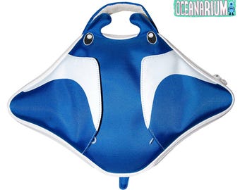 May include: Blue and white stingray-shaped bag with a handle. The bag features a zipper closure and a design that resembles a stingray's face, with eyes and a mouth. The text "Oceanarium" is visible in the upper right corner.