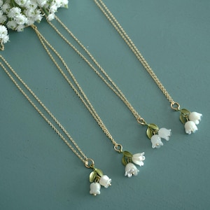 May include: Four gold necklaces with delicate lily of the valley flower charms. The charms are white with green leaves.