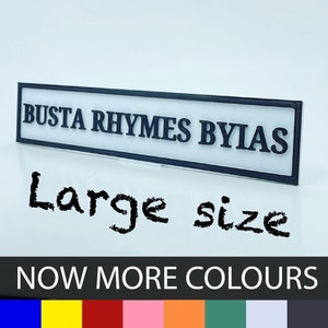 May include: A white rectangular sign with black text that reads "Busta Rhymes Byias". The sign is on a white background and the text "Large size" is written in black below the sign. The text "NOW MORE COLORS" is written in black below the text "Large size". A row of colored squares is below the text "NOW MORE COLORS".