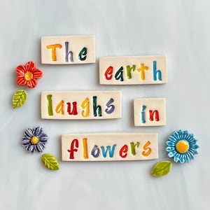 May include: Ceramic tiles with the words "The earth laughs in flowers" in colorful letters. The image also includes ceramic flower and leaf accents in red, blue, and green.