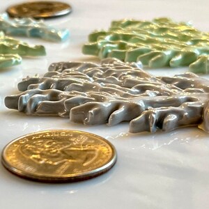 May include: A collection of ceramic decorative pieces in various colors, including light blue, green, and gray, arranged on a white surface. The pieces have a textured, organic design, and are accompanied by US currency coins.