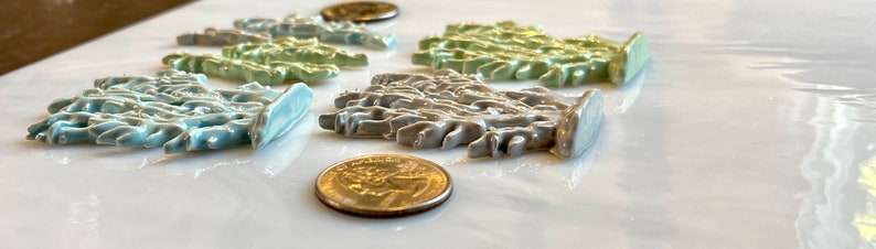 May include: A collection of ceramic decorative pieces in various colors, including light blue, green, and gray, arranged on a white surface. The pieces have a textured, organic design, and are accompanied by US currency coins.